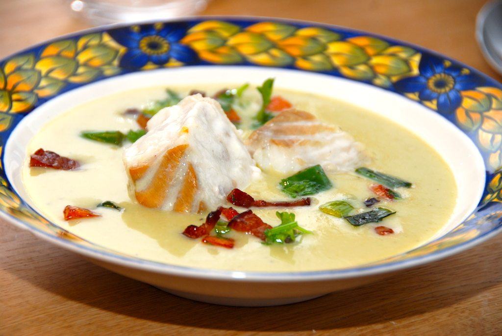 En lækker rosenkålssuppe med mørksej, der anrettes i dybe tallerkner med sprødstegt bacon og lidt grønt. Hæld suppen i den dybe tallerken, læg den ovnstegte fisk i midten, og drys lidt bacon og grøntsager rundt om. Foto: Guffeliguf.dk.