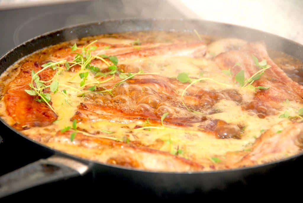 Den bedste spareribs opskrift, hvor flæskestykkerne brunes gevaldigt af på panden, hvorefter de krydres. Her er de dejlige spareribs ved at koge op på sammen sammen med krydderier og kyllingefond. derefter skal de steges i ovnen i en times tid. Foto: Madensverden.dk.