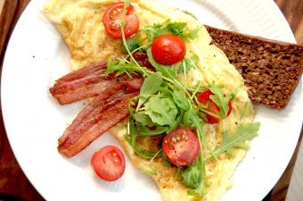 Sådan en omelet med rucola er en nem omelet til morgenbordet eller en brunch, og du skal beregne to æg pr. omelet. Her er omeletten serveret med sprødstegt bacon og små tomater. Foto: Madensverden.dk.