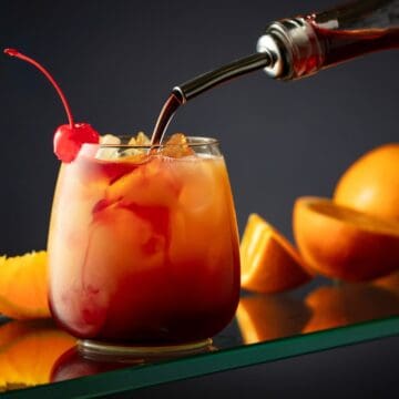 Rød grenadinesirup i en flaske og et glas, klar til brug i drinks og cocktails.